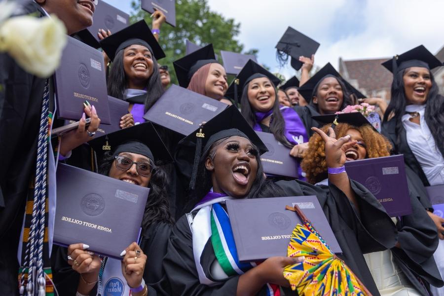 A group of students gather for a photo while holding their purple diplomas